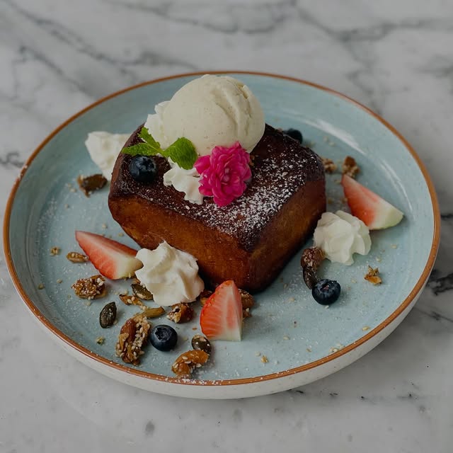 Caramelized brioche with vanilla ice cream, fresh berries, strawberry slices and an edible flower on a blue ceramic plate over marble