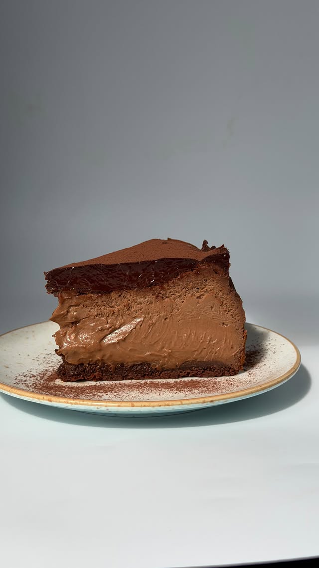 Chocolate cheesecake slice dusted with cocoa on a ceramic plate